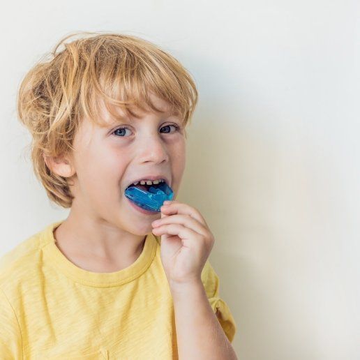 Young boy placing blue athletic mouthguard over his teeth