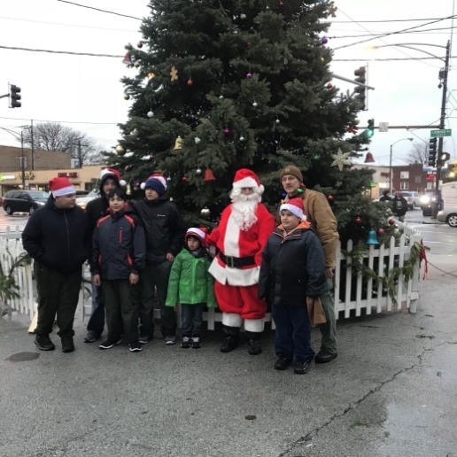 Whiting dentist dressed up as Santa standing in front of Christmas tree on sidewalk