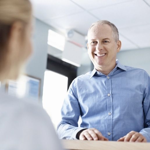 Man in light blue shirt talking to dental team member at front desk