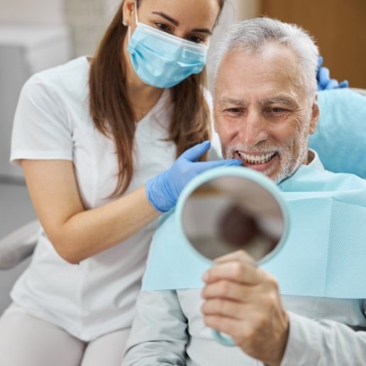 Senior man in dental chair looking at his smile in a mirror