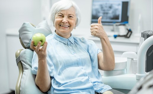 Woman sitting in patient’s chair holding an apple and smiling