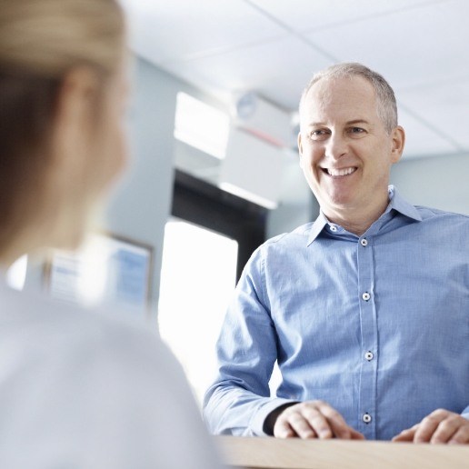 Man in light blue shirt talking to dental team member at front desk