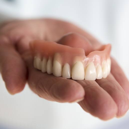 Dentist holding a full denture in Whiting in their hand