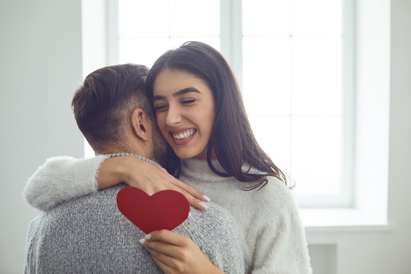 A woman hugging a man while holding a paper heart