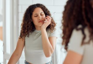 Woman brushing teeth, holding mouth in pain.