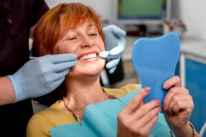 Woman looking at dentures in mirror in dentist's chair.